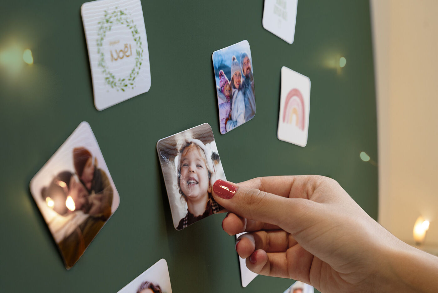 Plusieurs magnets personnalisés aimantés sur un tableau et une main posant un magnet photo