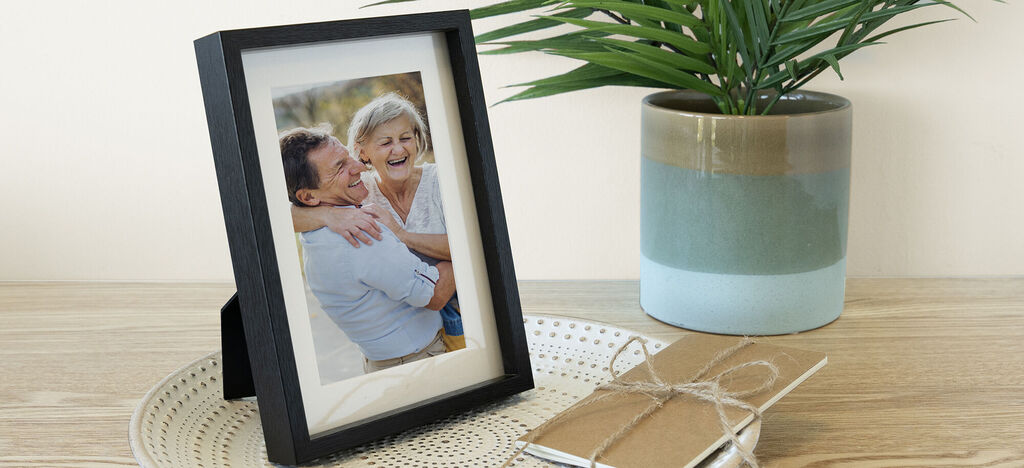 Une belle photo encadrée d'une étreinte aimante sur une table. Un carnet et une plante sont à côté.