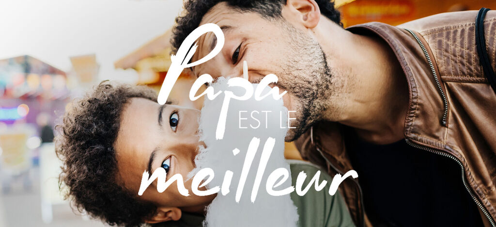 Un adulte sourit affectueusement à un enfant qui se tient près de lui, dans un environnement joyeux.