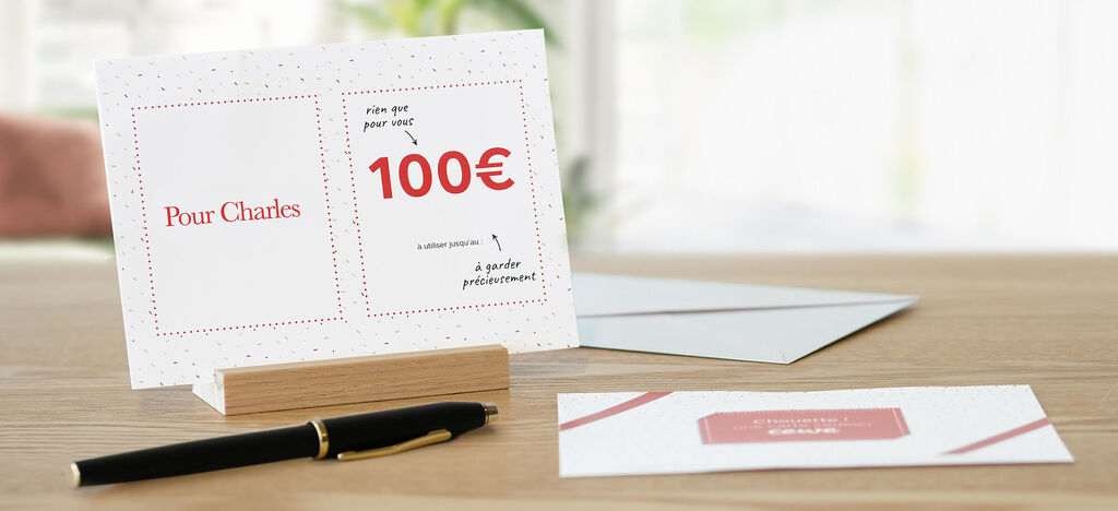 Cartes de vœux CEWE avec un message de 100€ sur une table, décorée avec un stylo et des enveloppes.