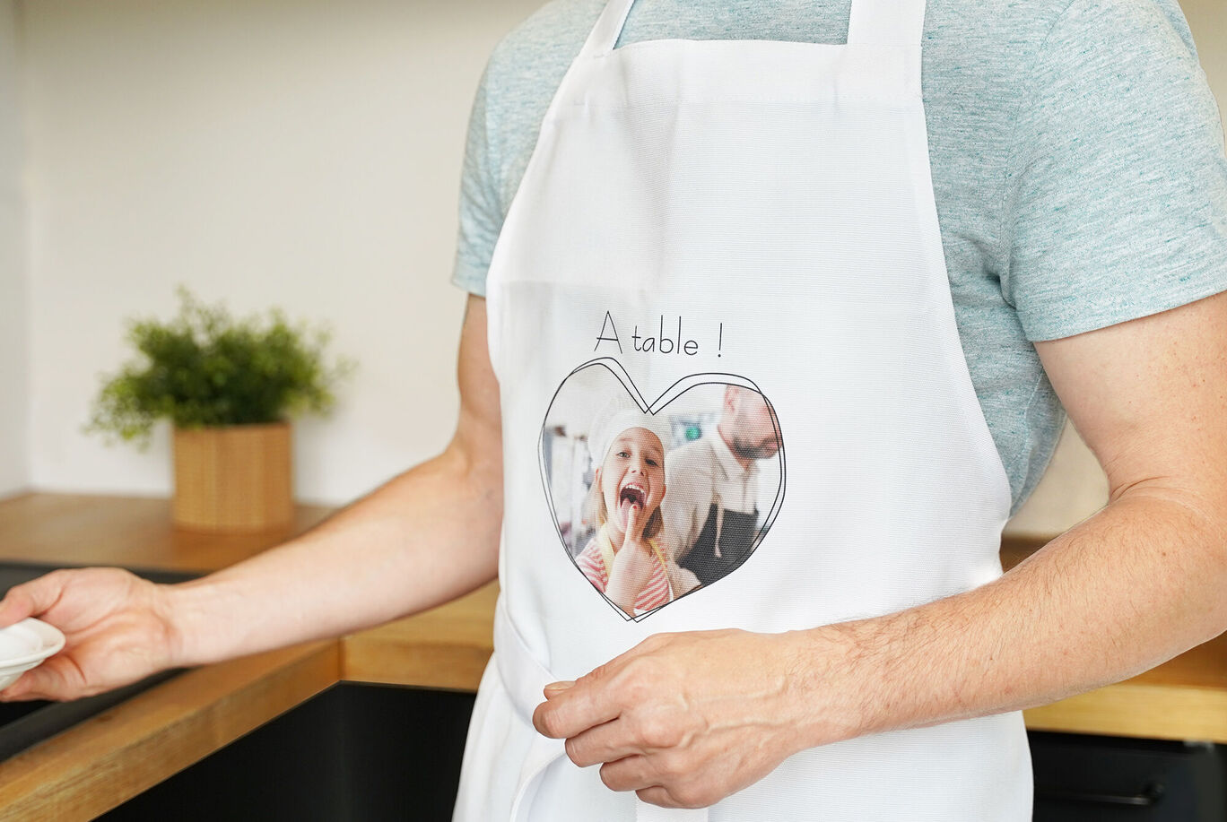 Un homme porte un tablier avec une photo en forme de cœur et le texte 'A table!' sur la poitrine.