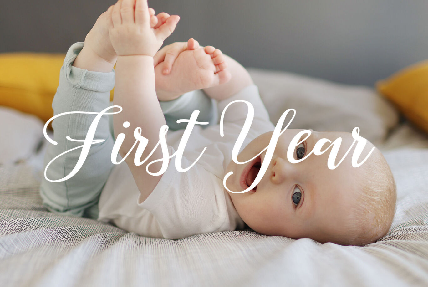 Un bébé est sur le dos, jouant avec ses jambes sur un lit. Des oreillers jaunes sont visibles en arrière-plan.