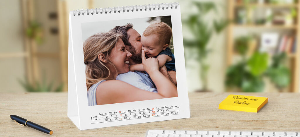 Un calendrier photo CEWE soigneusement conçu sur un bureau en bois, avec une photo de famille chaleureuse.
