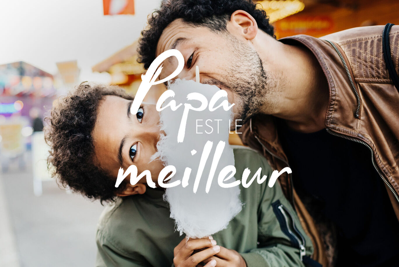 Un enfant joyeux déguste de la barbe à papa et regarde l'objectif, tandis qu'un adulte lui sourit avec tendresse